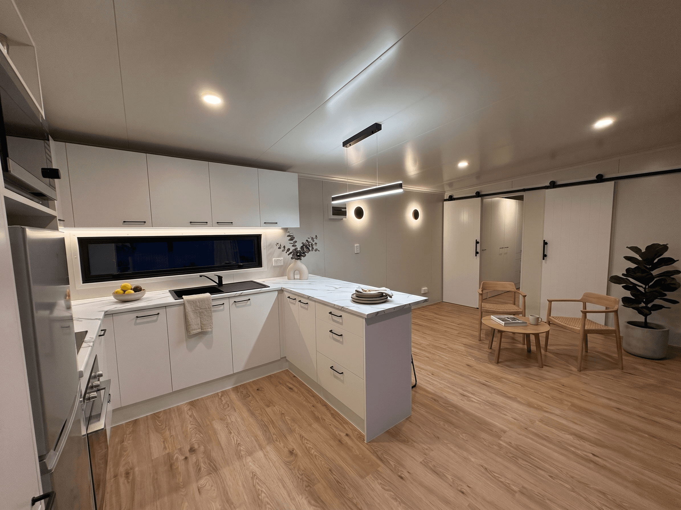 Open-plan transportable home kitchen and living with marble benchtop and dining nook