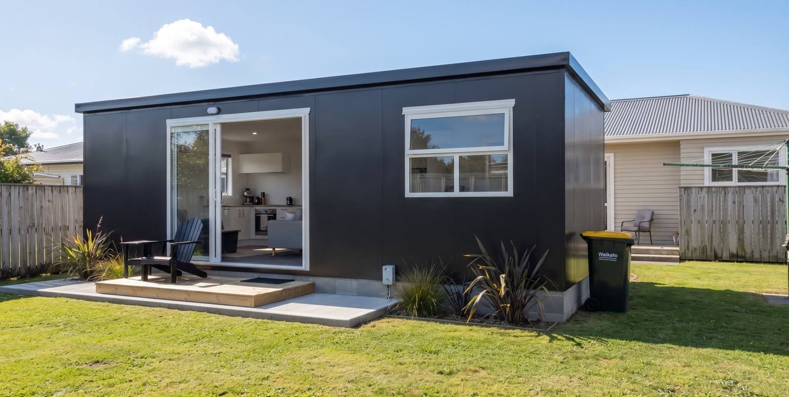 Black 8×3 economy one-bedroom tiny home with white-trimmed sliding door and window on a timber deck