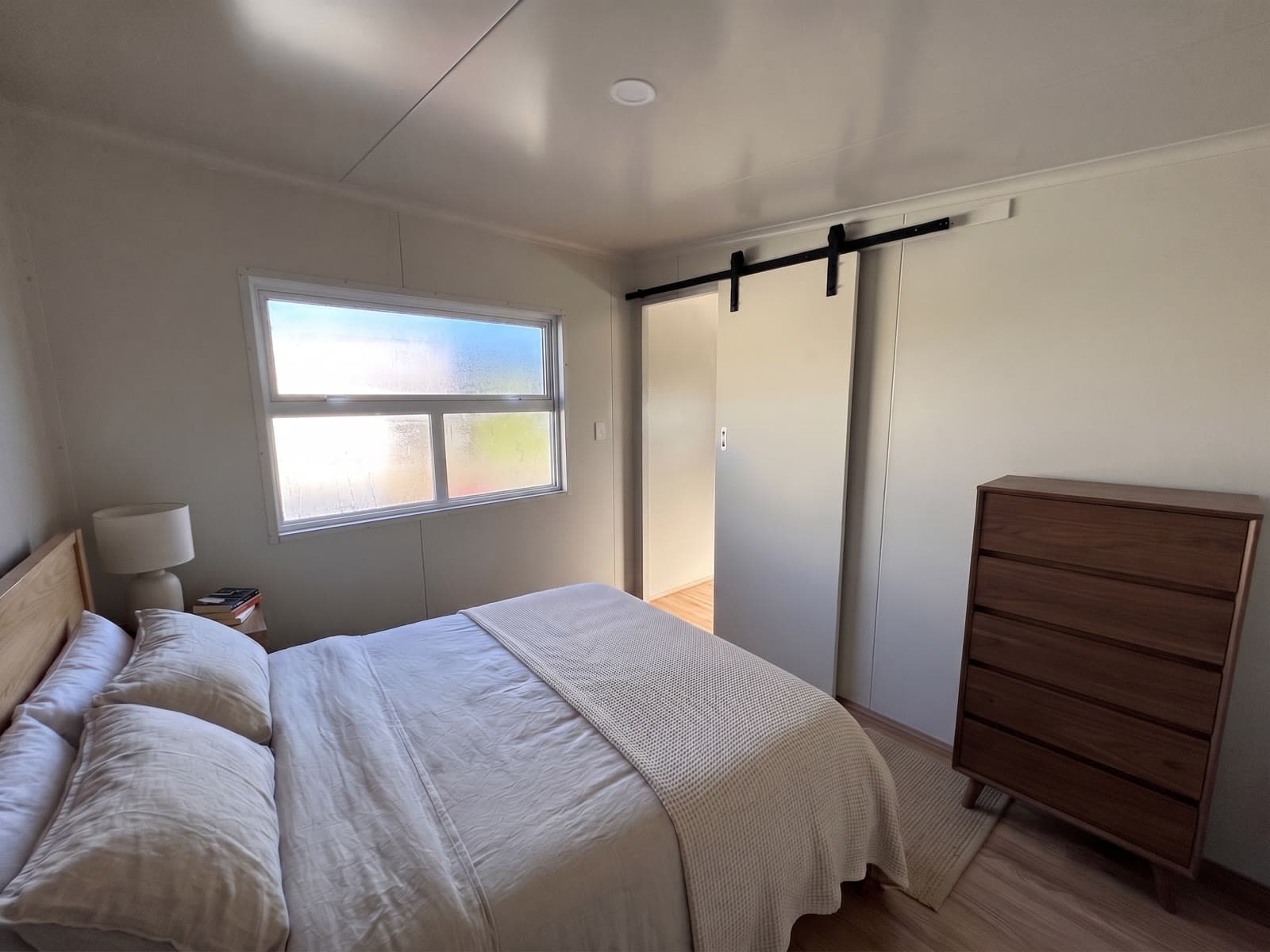 8×3 tiny home bedroom with queen bed, barn-style sliding door to the bathroom and timber tallboy