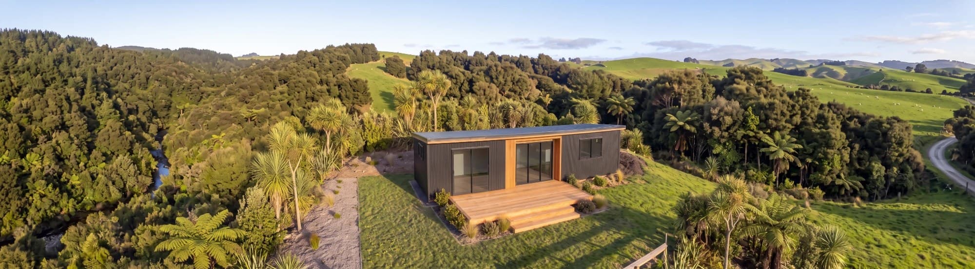 Dark-clad NZ-made tiny home with timber feature cladding and deck on a native bush hillside