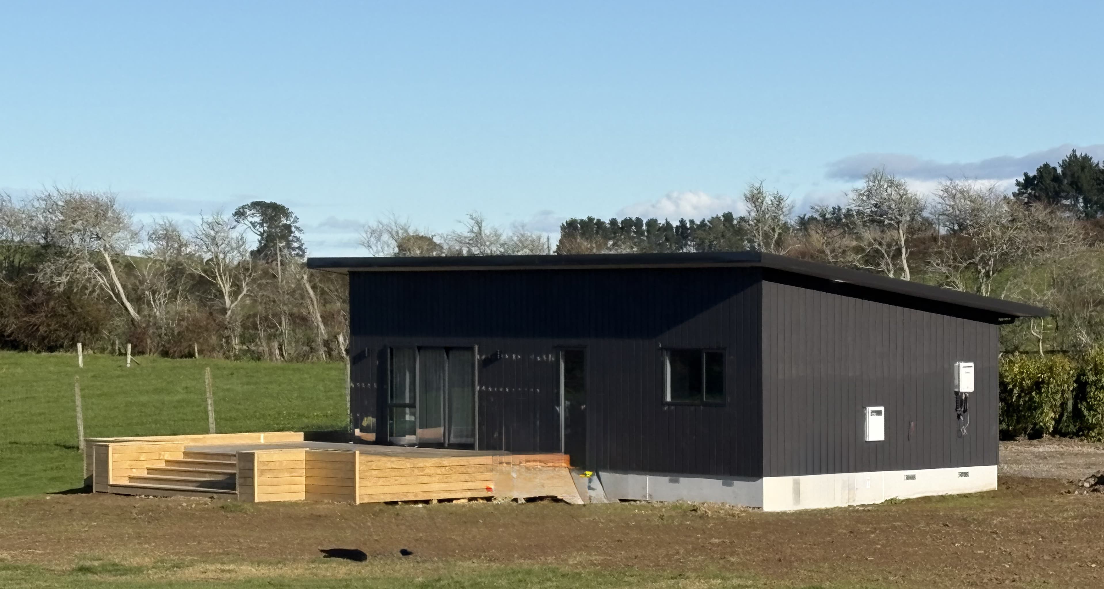 Black NZ-made transportable home with timber deck as farm staff accommodation on a Te Kowhai property